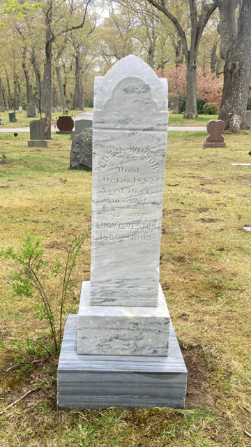 White marble gravestone in a grassy cemetery with trees in the background