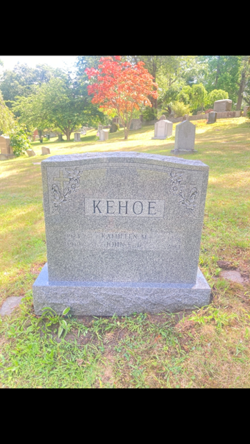 Gray KEHOE gravestone in a sunny cemetery with green grass and autumn trees.