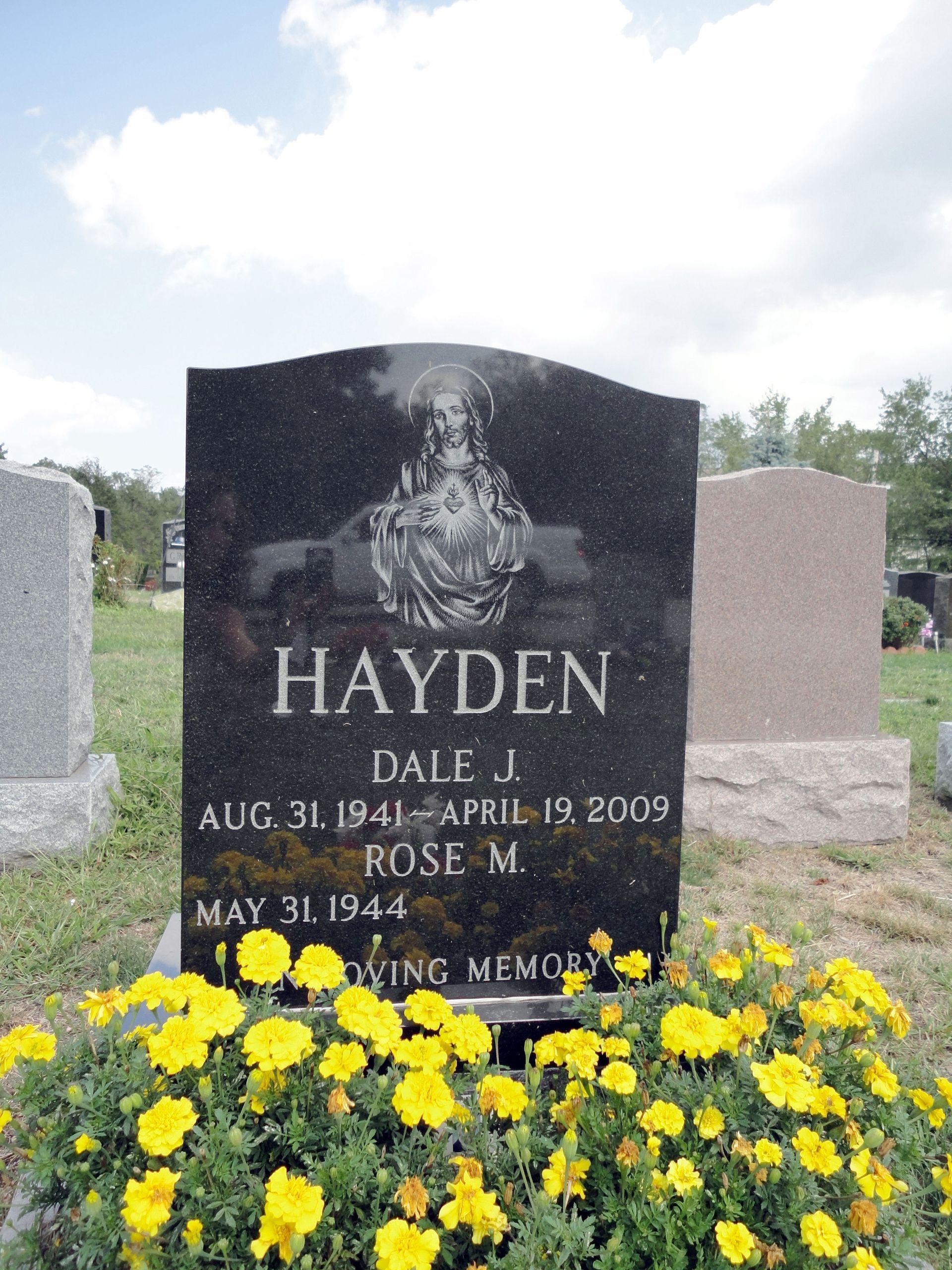 Black headstone for Hayden with yellow flowers at the base in a cemetery.