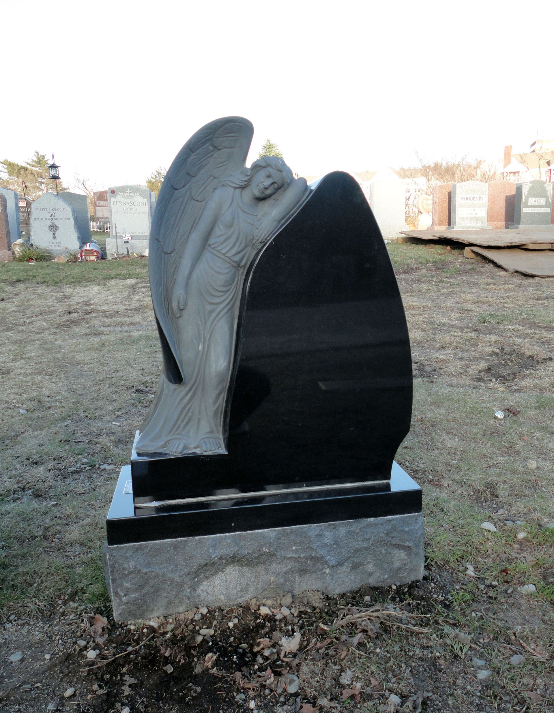 Black granite memorial monument with sculpted angel wings on a stone base outdoors