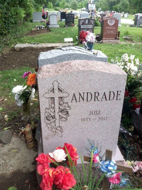 Gravestone engraved “ANDRADE” in a cemetery, with red and white flowers at the base.