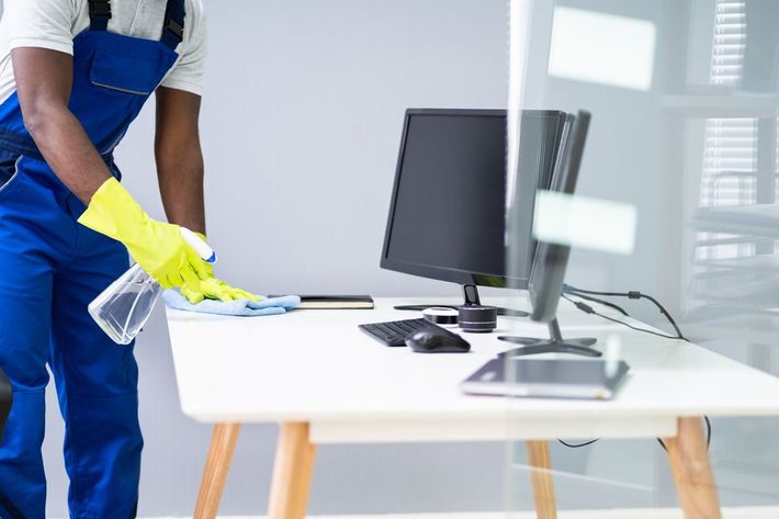 A man is cleaning a desk with a computer on it A man is cleaning a desk with a computer on it