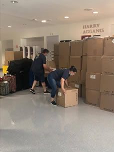 A man and a woman are lifting a box in a room filled with boxes