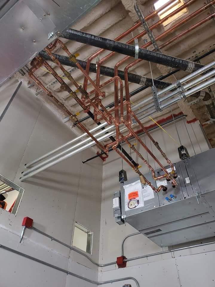 Ceiling-mounted pipes and electrical conduits above industrial equipment in a utility room