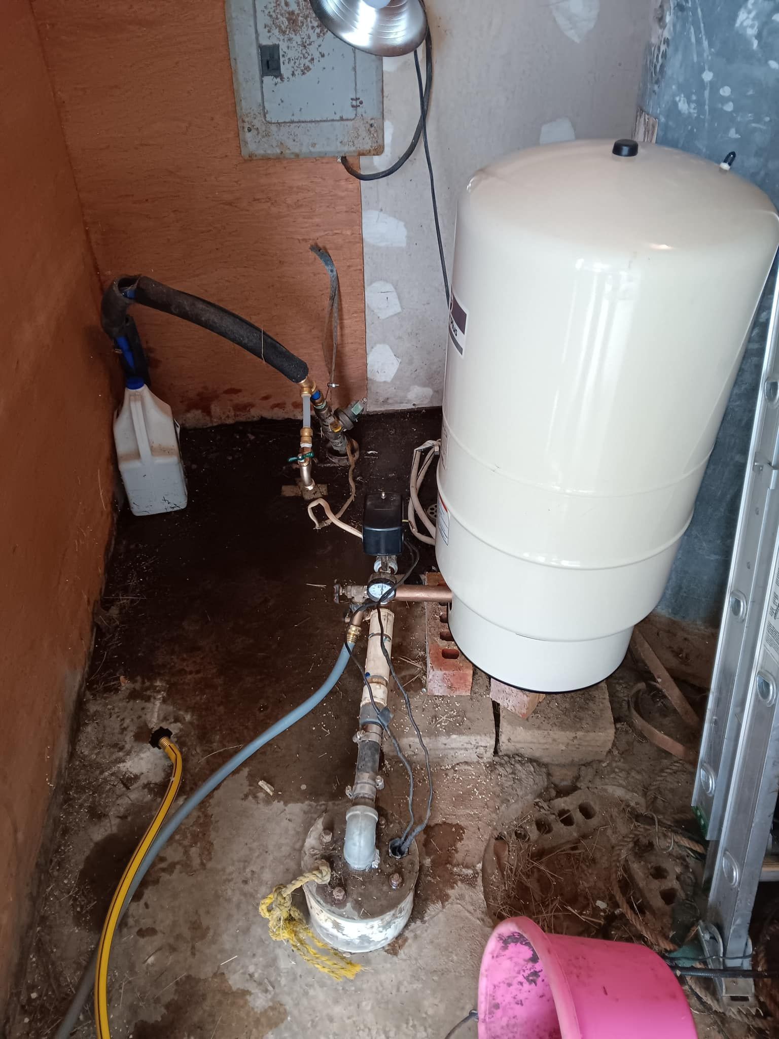 Plumbing area with a white water heater tank, exposed pipes, and a damaged floor around the base.