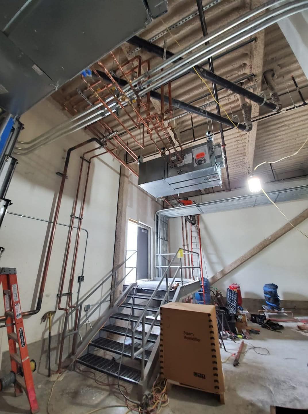 Construction site with exposed ceiling beams, scaffolding, stairs, and workers in an unfinished room.