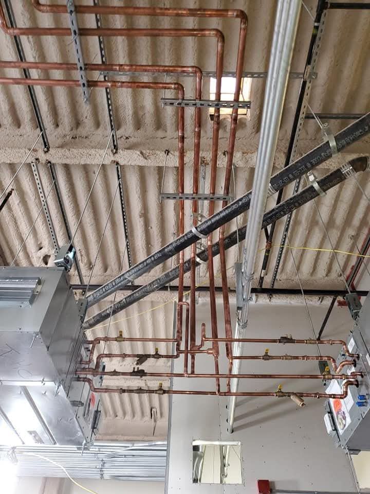 Industrial ceiling with exposed red and black pipes, ducts, and corrugated metal roof panels.