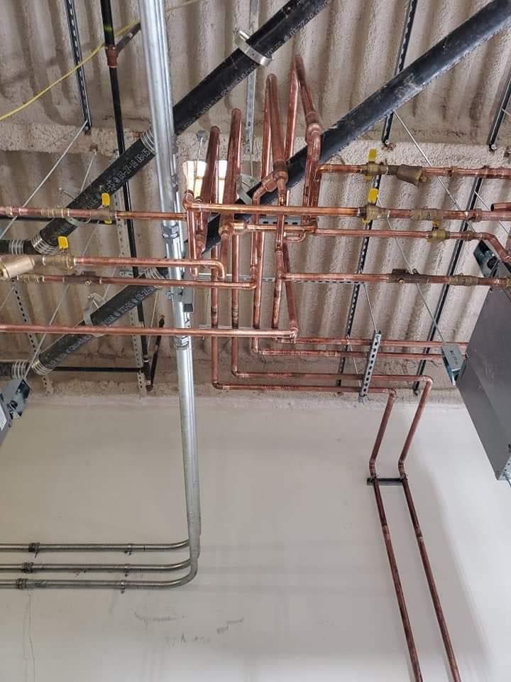 Exposed ceiling with copper and gray pipes and conduit in an unfinished interior