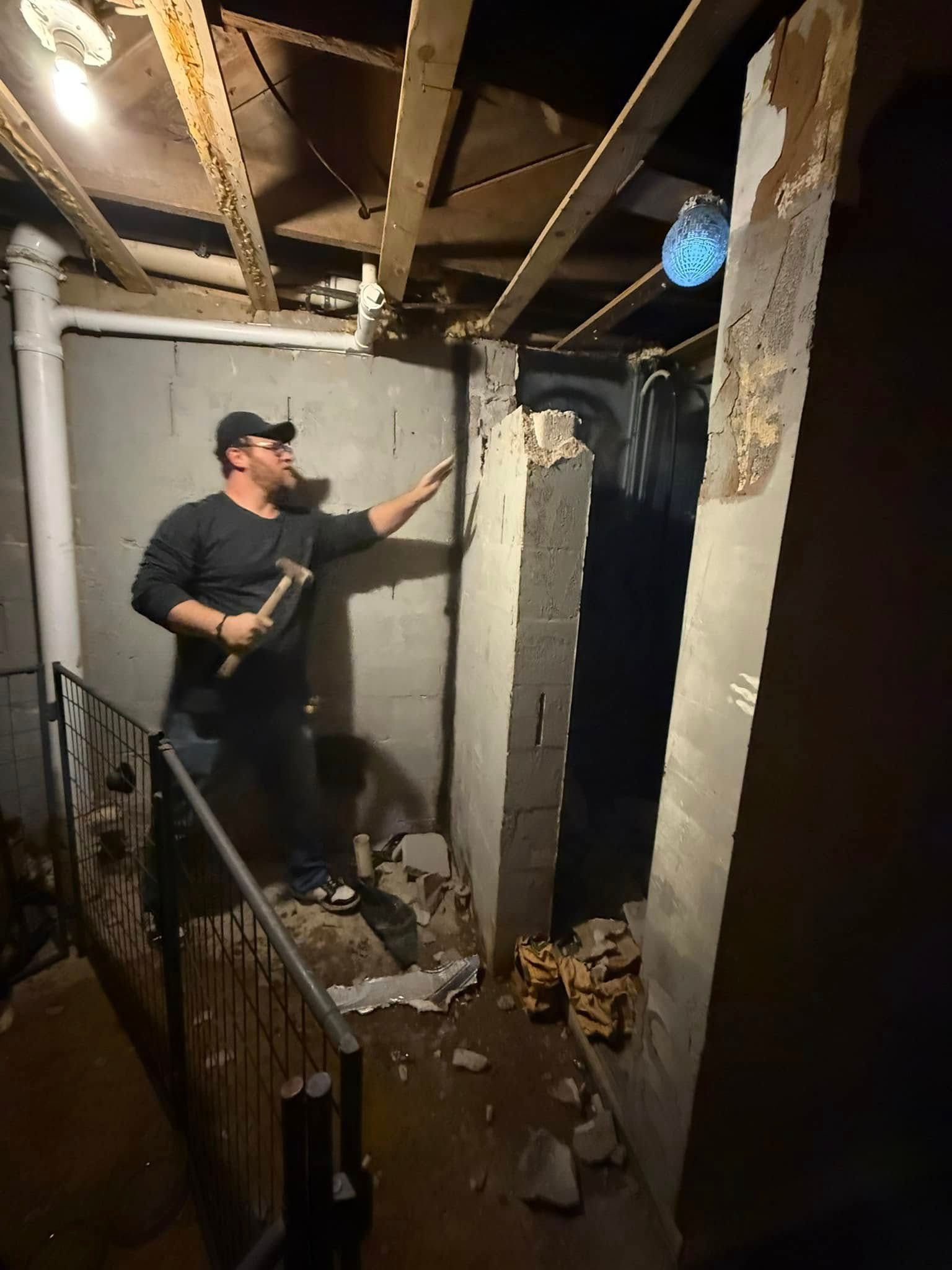 Worker holding a tool in a damaged room with exposed ceiling joists and debris on the floor