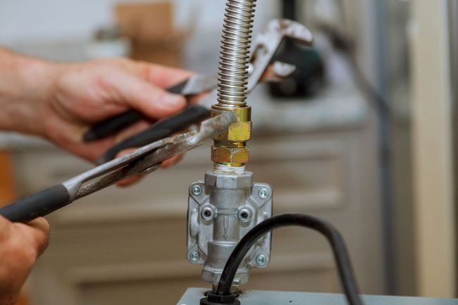 Hands using pliers to tighten a gas valve on a metal pipe assembly