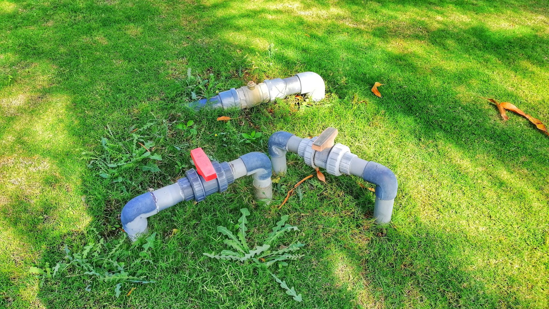 Plastic pipe fittings arranged on green grass in a yard, including a red valve and gray elbows