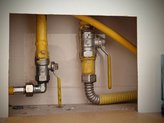 Two exposed gas pipes with yellow shutoff valves inside a wall opening