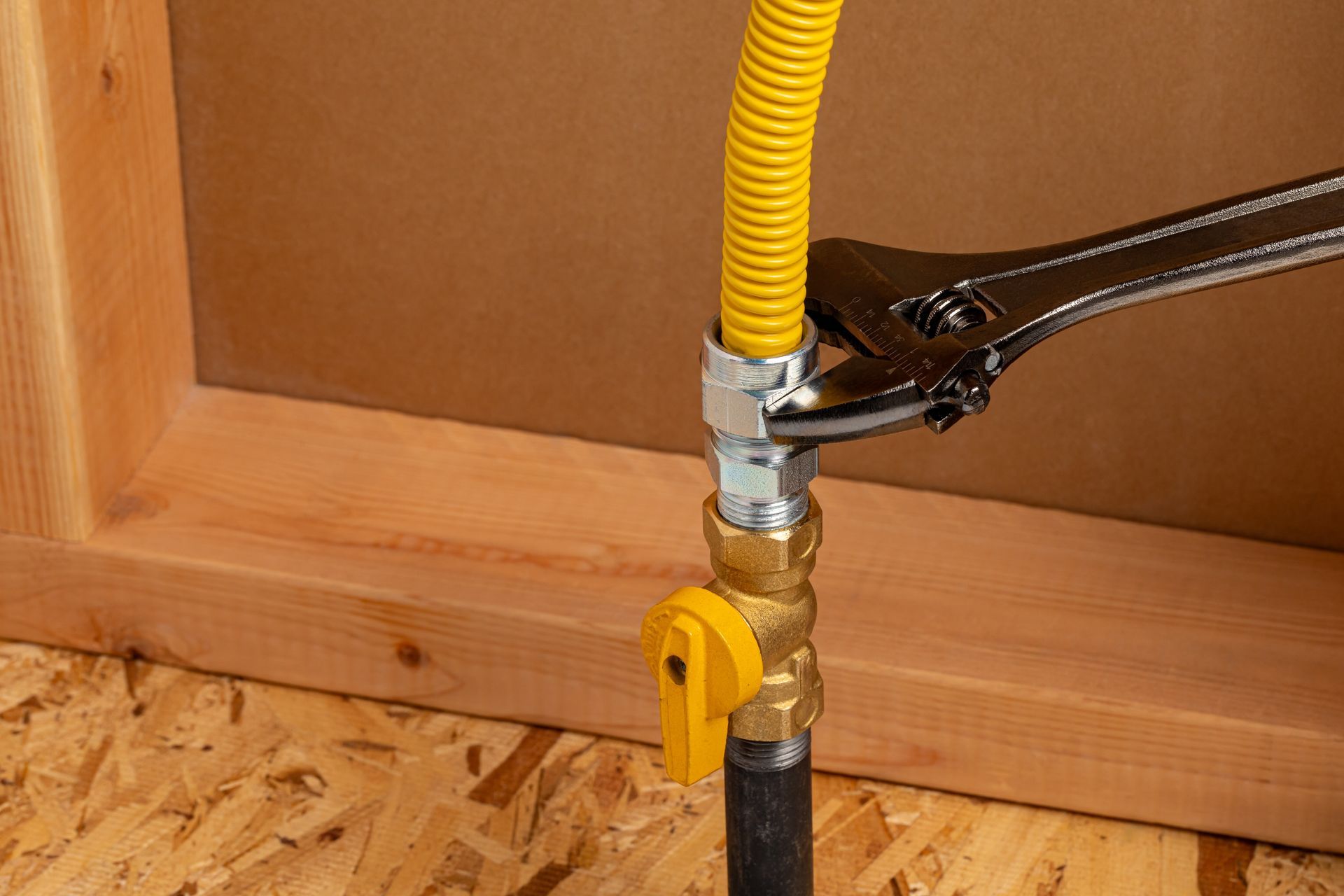 Yellow gas line and shutoff valve connected to a black pipe, being tightened with pliers.
