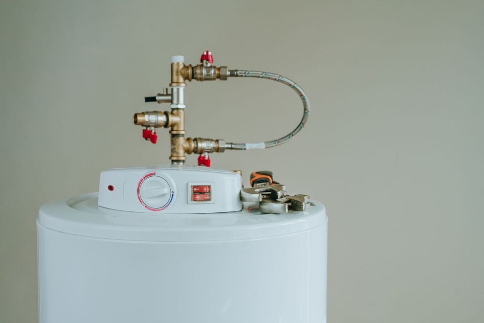 Small white appliance with brass valves, red knobs, and a looping hose on a white tank.