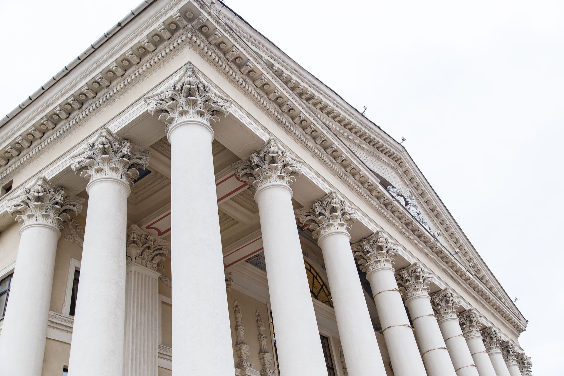 White classical building with tall columns and ornate capitals, under a cloudy sky.
