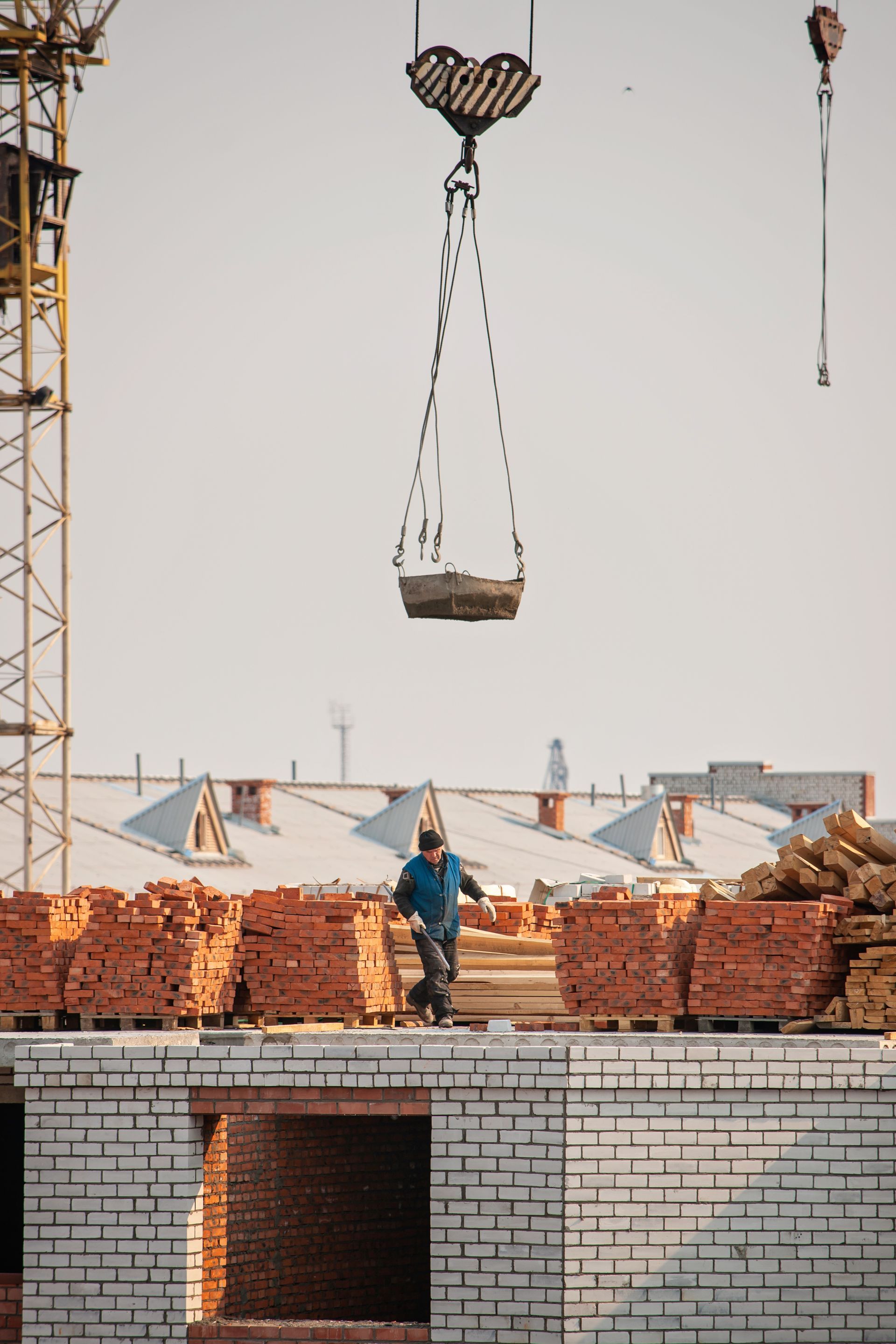 Construction worker on rooftop receiving bricks from a crane.