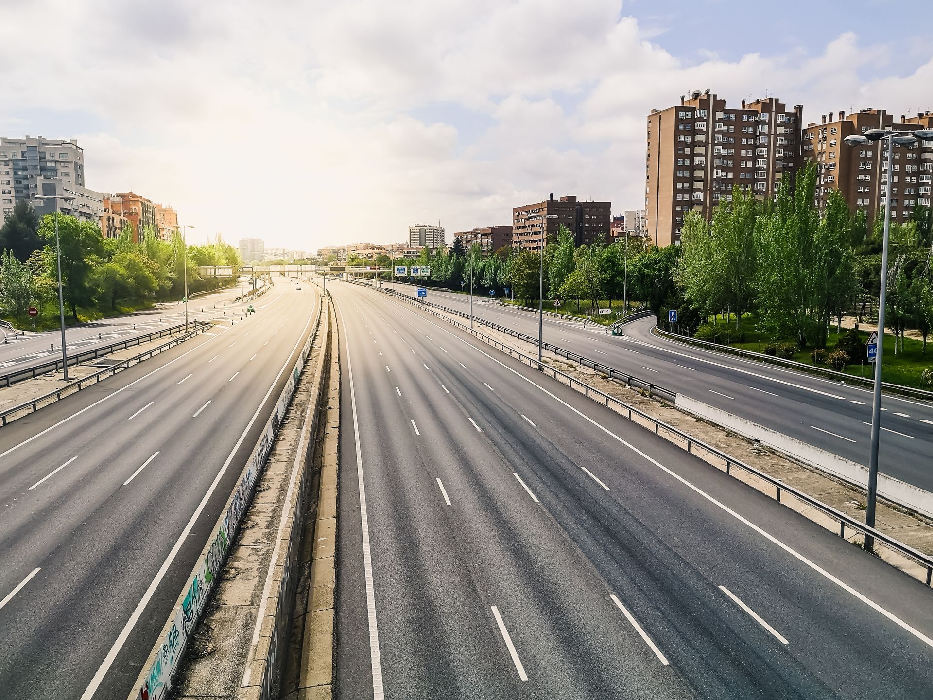 Empty multi-lane highway in city with buildings and trees, sunny day.