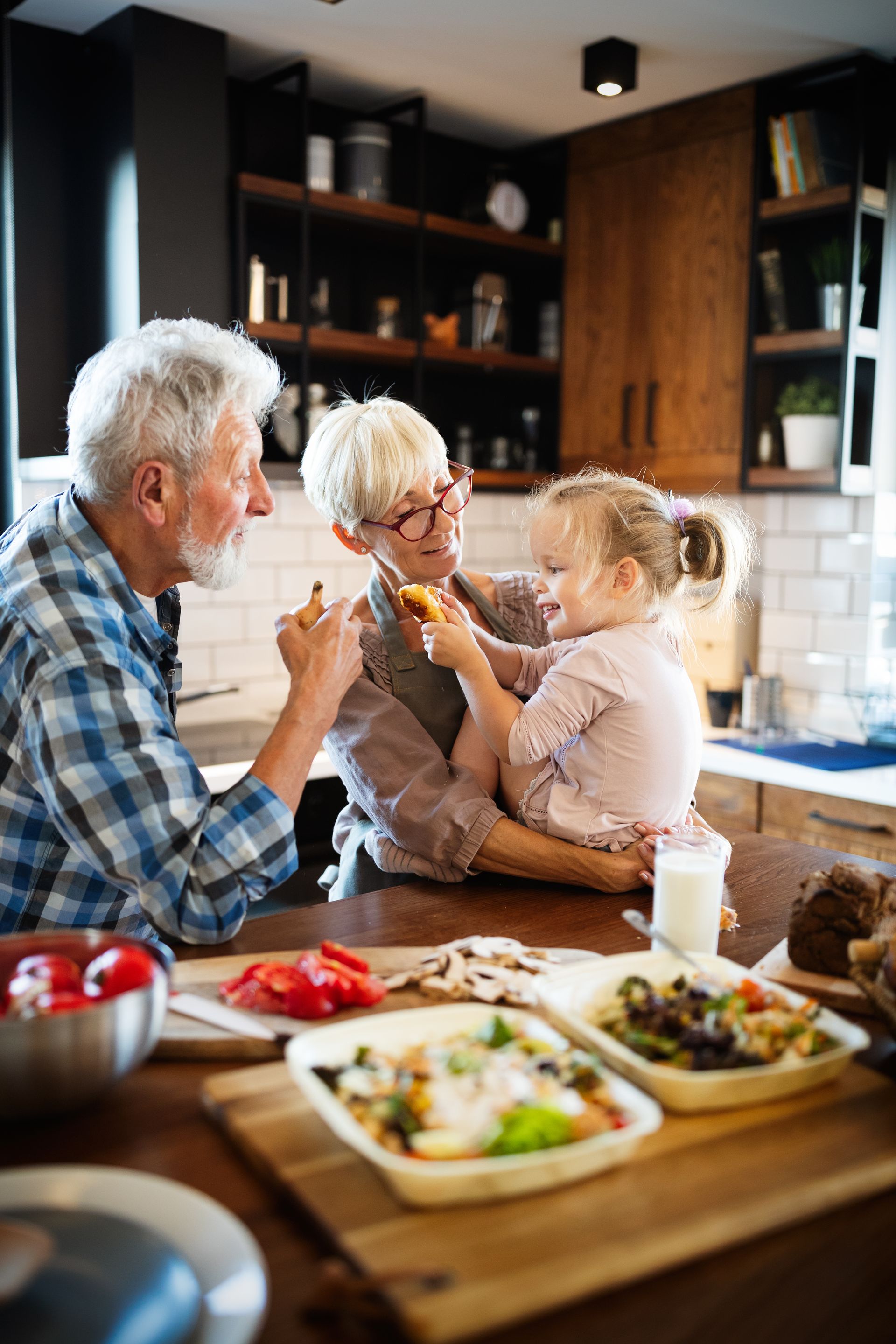 Grandparents and grandchild prepare food together in a kitchen, sharing a playful moment.