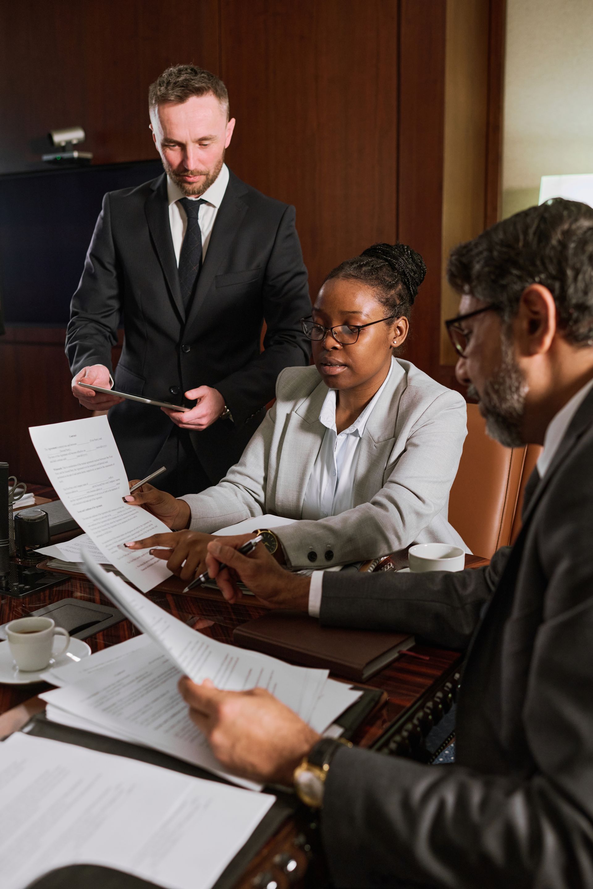 Three people in business attire reviewing documents at a table. One holds a clipboard.