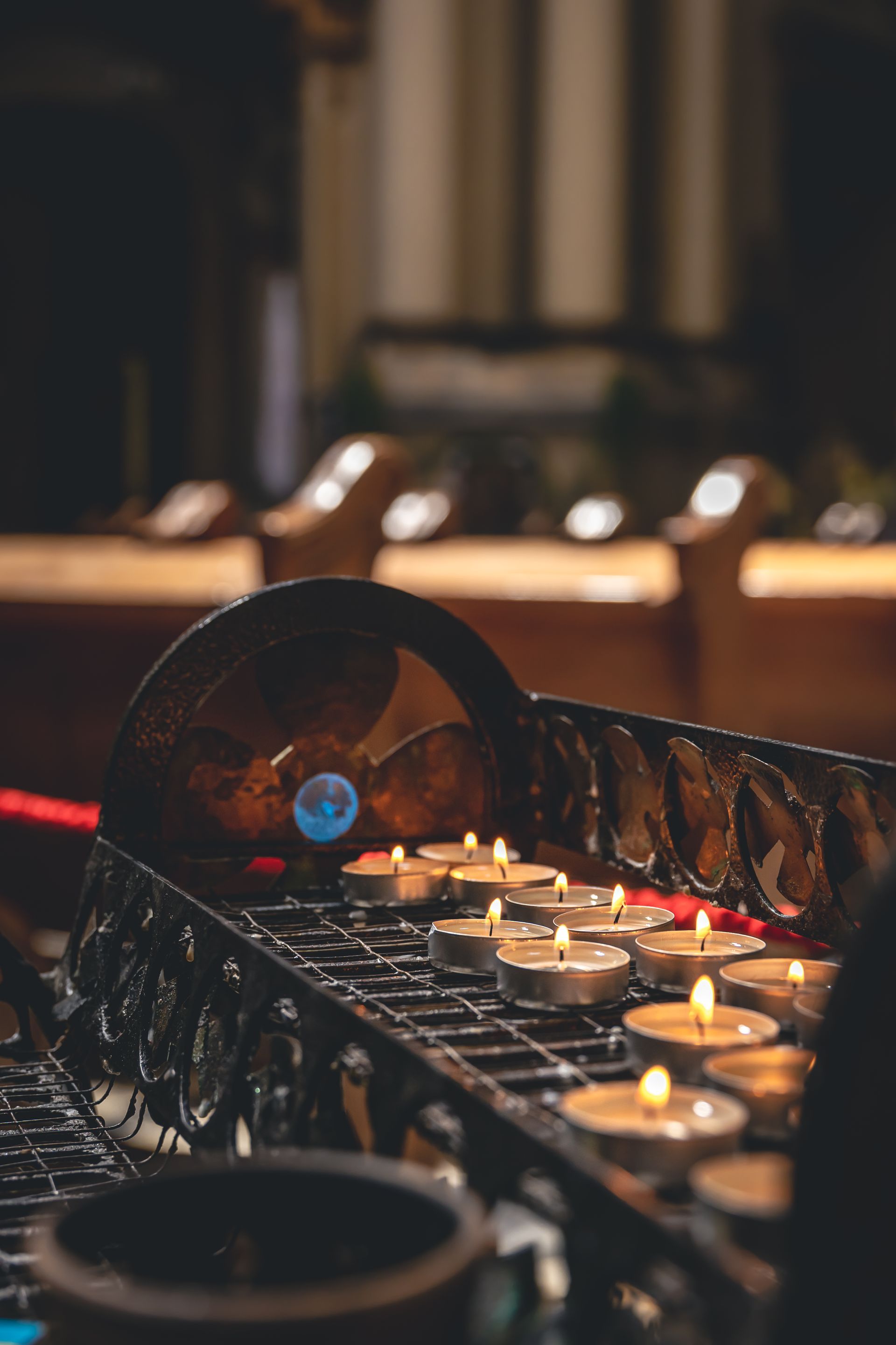 Candle rack with lit votive candles in a church, with a blue flame lighting them.