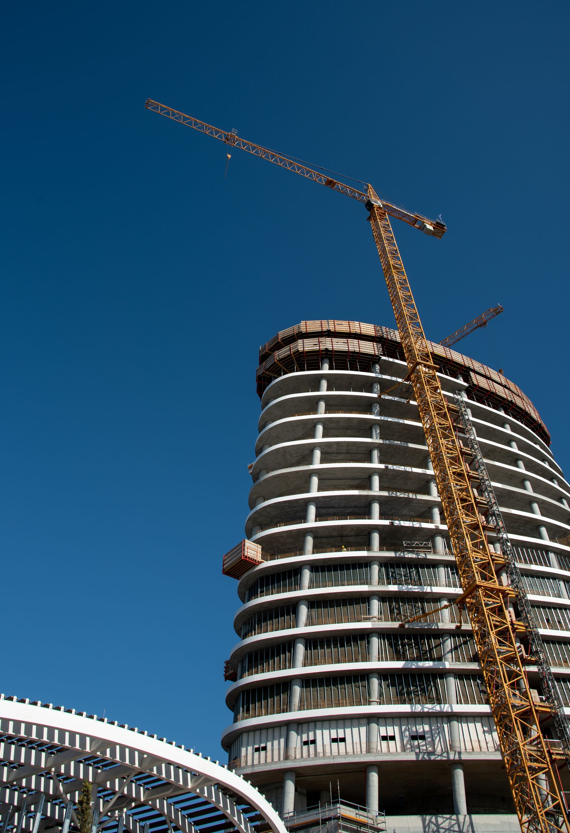 Construction of a modern, curved skyscraper with a yellow crane against a clear blue sky.