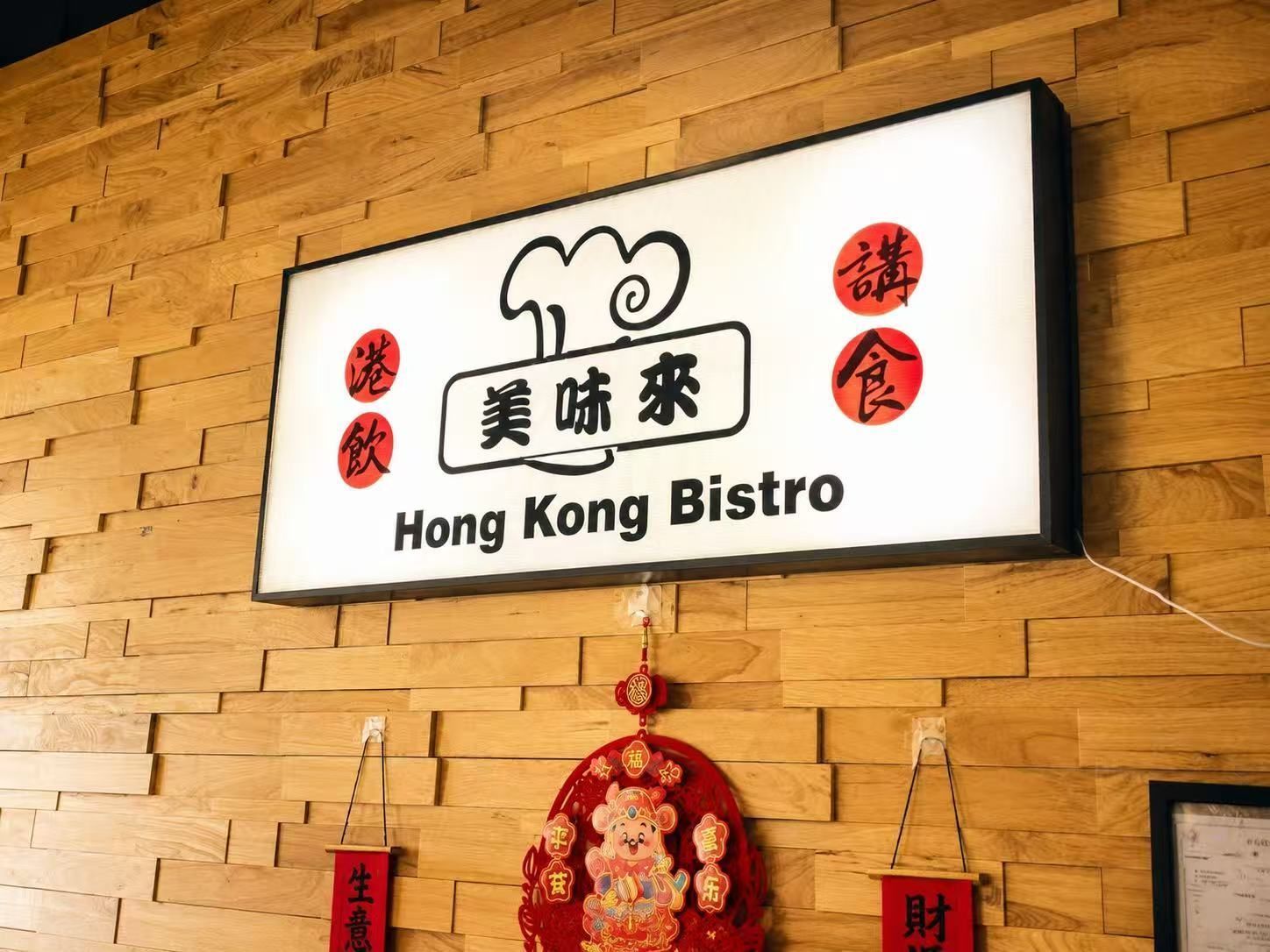 Hong Kong Bistro sign on a tan brick wall with red hanging decorations