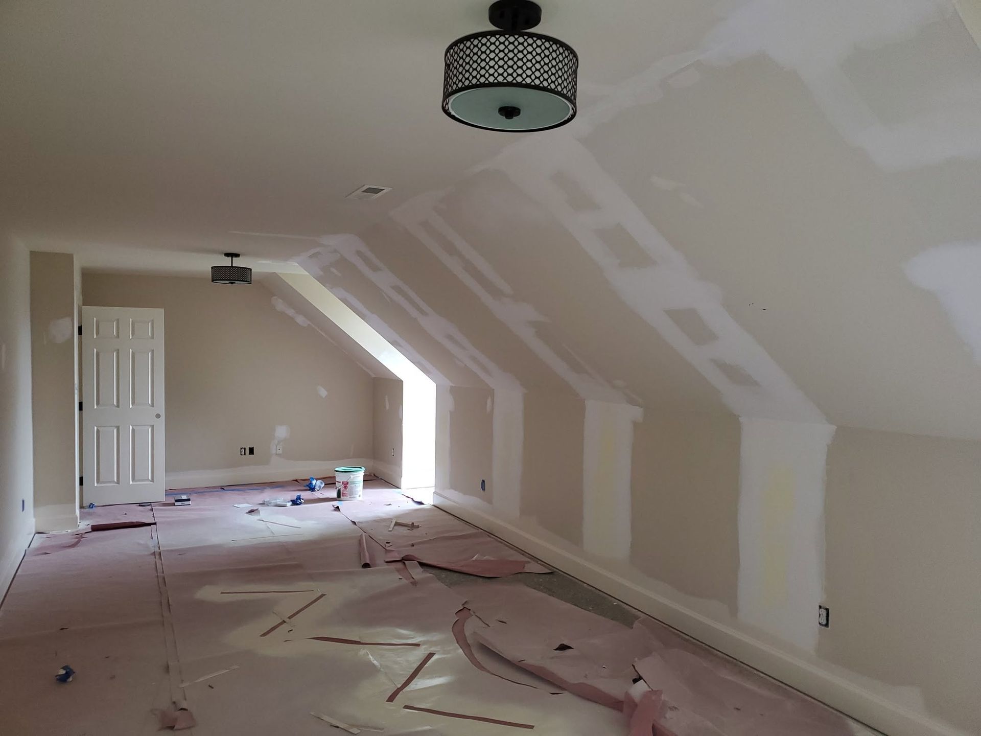 Partially renovated attic room with drywall patches, white walls, and a bare floor
