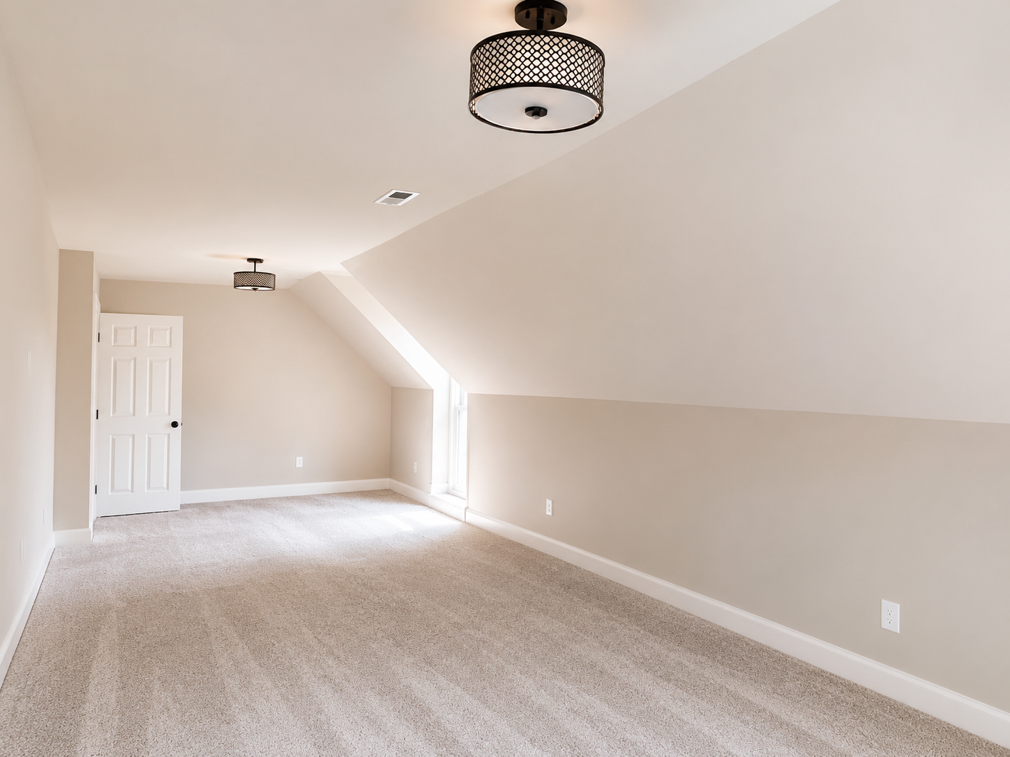 Empty beige carpeted room with sloped ceiling, white door, and two ceiling lights