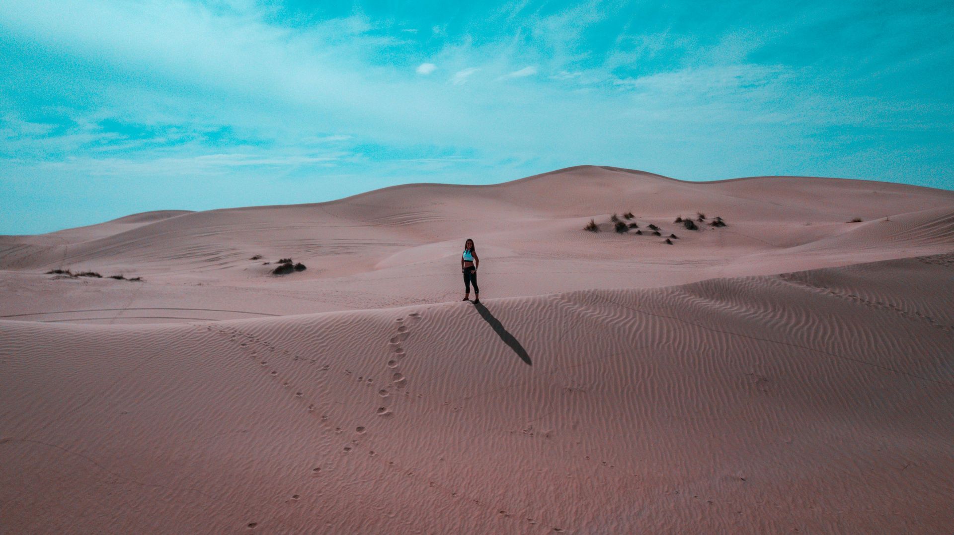 A person is standing on top of a sand dune in the desert.