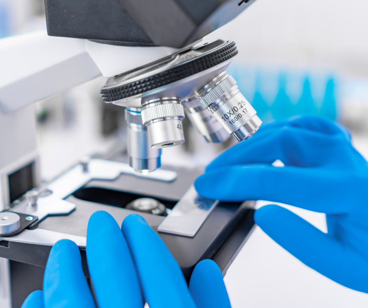 A person wearing blue gloves is looking through a microscope