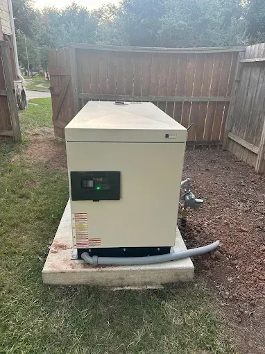Beige generator on a concrete pad beside a wooden fence in a backyard.