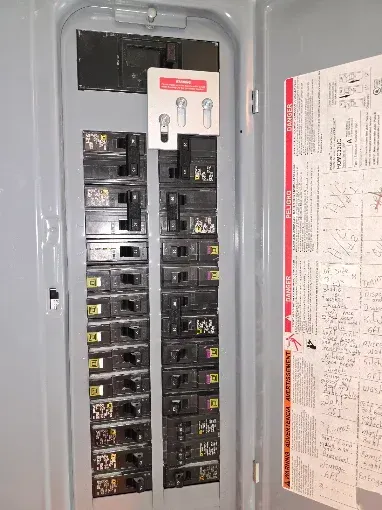 Open electrical breaker panel with rows of black switches and a circuit map on the inside door.
