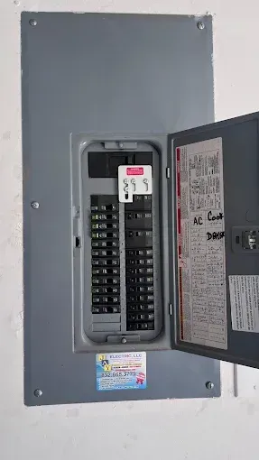 Open electrical breaker panel with gray metal door and rows of black switches.