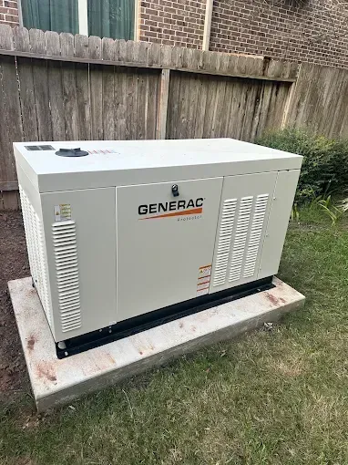 Generac home standby generator on a concrete pad beside a wooden fence in a grassy yard