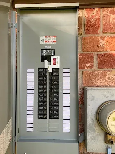 Open electrical breaker panel with wires and circuit breakers inside a wall-mounted cabinet