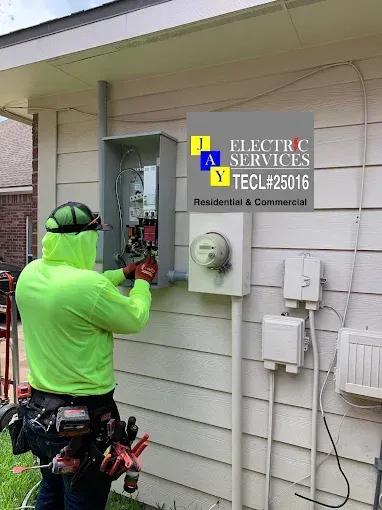 Worker in neon green jacket inspects exterior electric service panel on house wall.