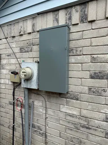 Gray utility boxes mounted on a brick house exterior with power lines and a meter fixture