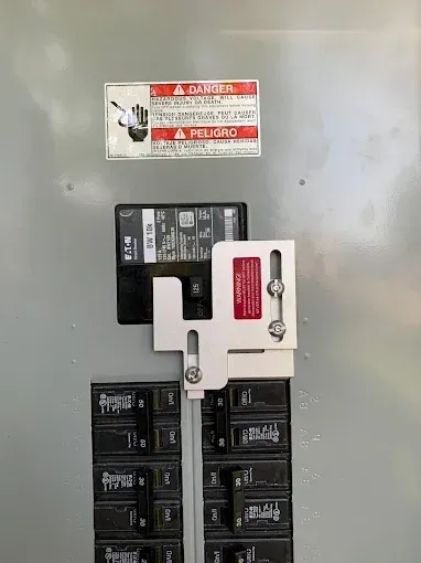 Electrical breaker panel with black switches and a red warning label on a gray wall