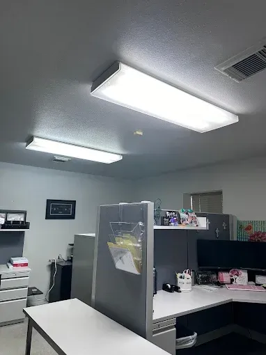Office cubicles with desks, computer monitors, and bright fluorescent ceiling lights