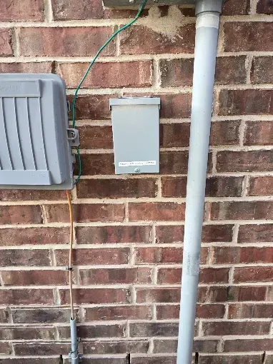 Brick wall with a gray utility box, cable, and white pipe outdoors