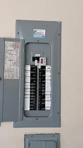 Open electrical breaker panel on a beige wall with rows of black and white switches.