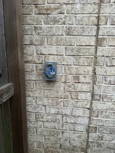 Blue wall-mounted box on a light brick exterior wall beside a wooden fence post.