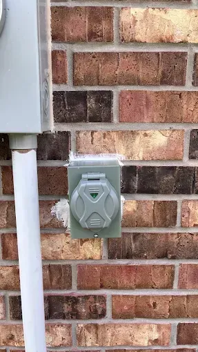 Outdoor electrical outlet box mounted on a brick wall beside a white downspout.