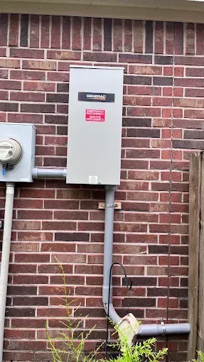 Gray electrical control panel mounted on a brick wall with conduit pipes running below
