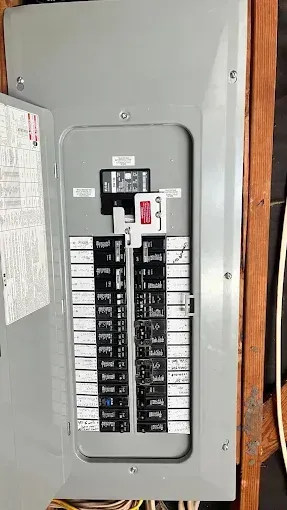 Open electrical breaker panel with rows of switches and labels on a gray wall
