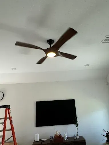 Living room with a modern ceiling fan, wall-mounted TV, ladder, and wooden console table