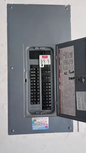 Open electrical breaker panel with black switches and door ajar on a gray wall