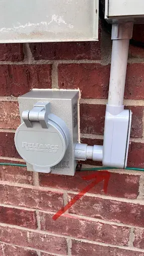 Gray electrical box and conduit mounted on a red brick wall near the ground