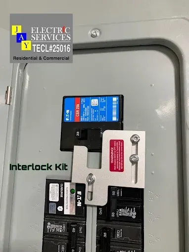 Electrical service panel with interlock kit installed, showing breakers and safety labels.