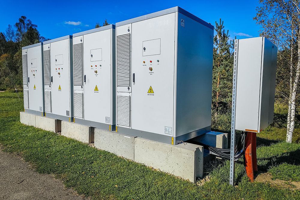 Outdoor electrical cabinets and utility equipment on a concrete pad beside grass, under a blue sky